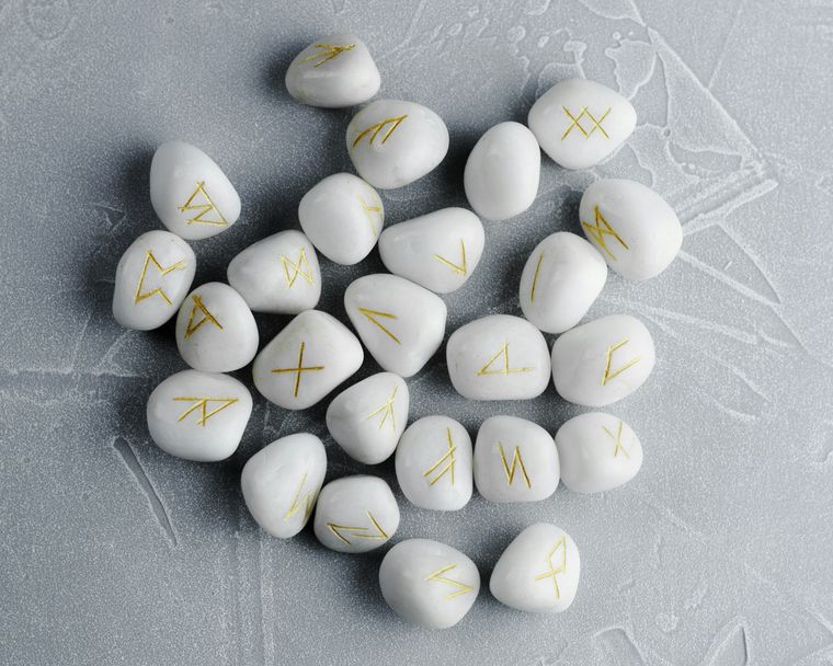 A bunch of white stones with yellow runes written on them lying on a grey surface